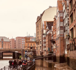 Historische Altstadth&auml;user entlang eines Kanals in Hamburg mit Spazierg&auml;ngern auf der Uferpromenade an einem bew&ouml;lkten Tag.