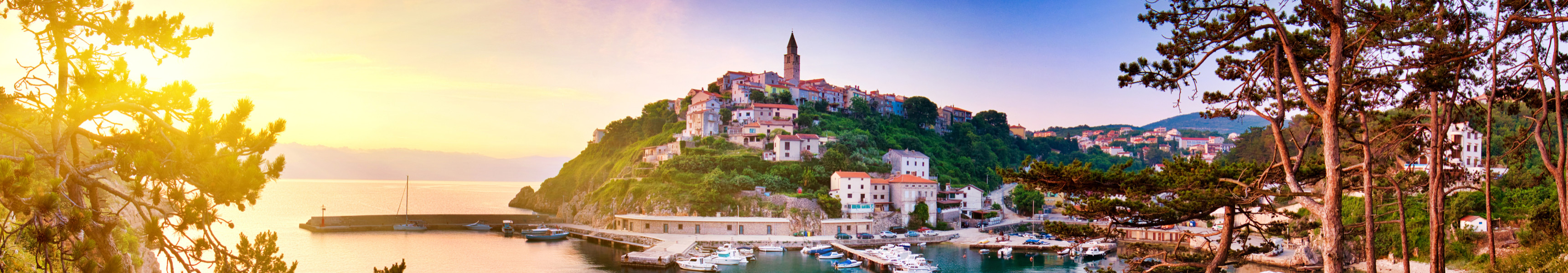 Sonnenuntergang über der Küstenstadt Vrbnik auf der Insel Krk in Kroatien mit Blick auf den Hafen, bunte Häuser und den markanten Kirchturm.