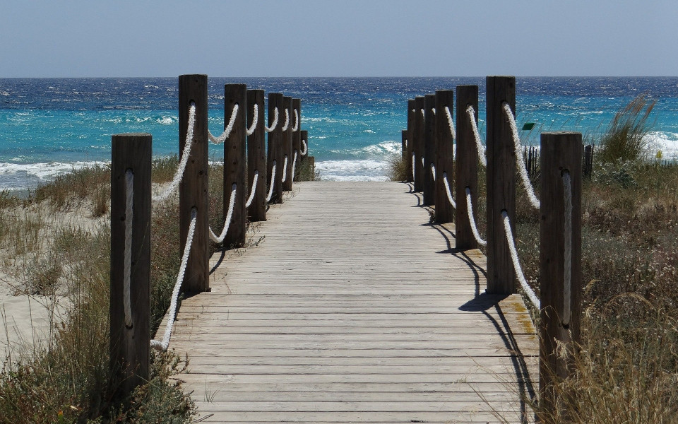 Ein Holzsteg führt vom Land zum Meer, mit Blick auf das azurblaue Wasser von Menorca.