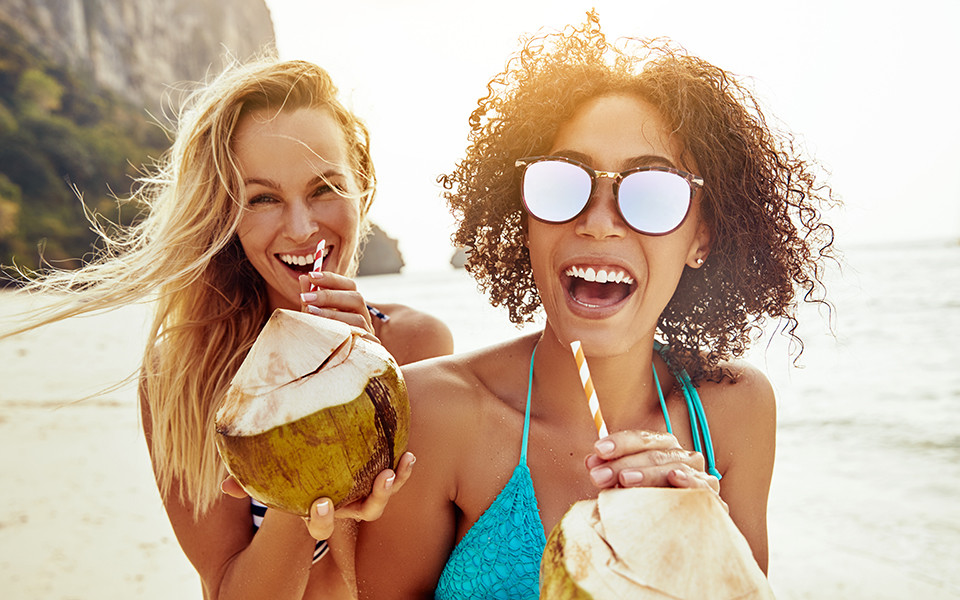 Zwei Frauen mit Kokosnuss in der Hand am Meer genie&szlig;en Fr&uuml;hbucher Reise