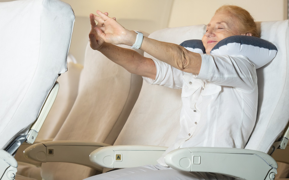 Tipps für entspanntes Fliegen: Ältere Frau dehnt und streckt sich am Platz