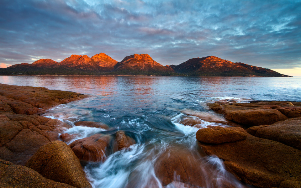 Sonnenuntergang &uuml;ber den Gefahren mit Alpengl&uuml;hen und flie&szlig;endem Wasser &uuml;ber Felsen, Freycinet-Nationalpark, Coles Bay, Tasmanien, Australien