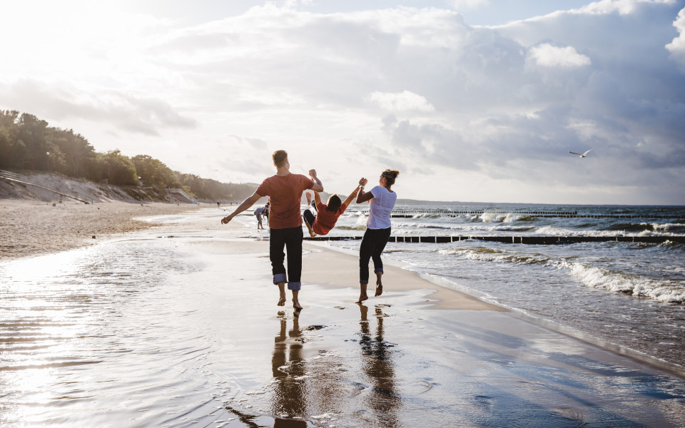 Familie läuft am Strand entlang und spielen mit ihrem Kind