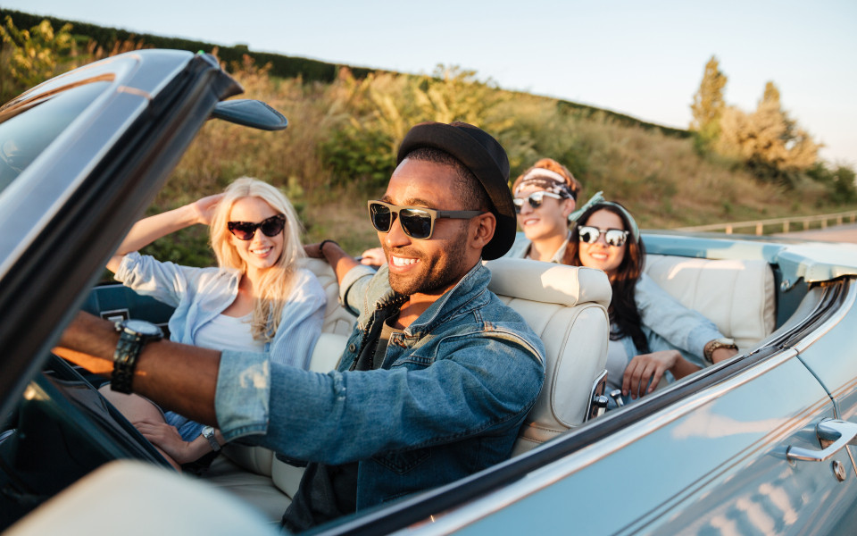 Fr&ouml;hliche junge Freunde fahren im Sommer Auto und l&auml;cheln.